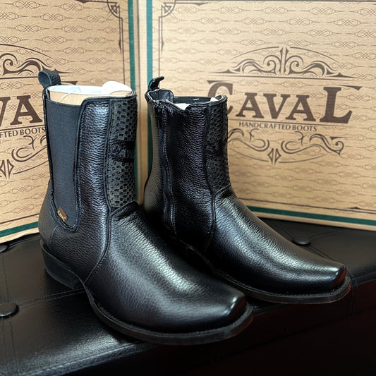 Black leather boots with white soles on a wooden surface in front of a 'Caval' branded box.