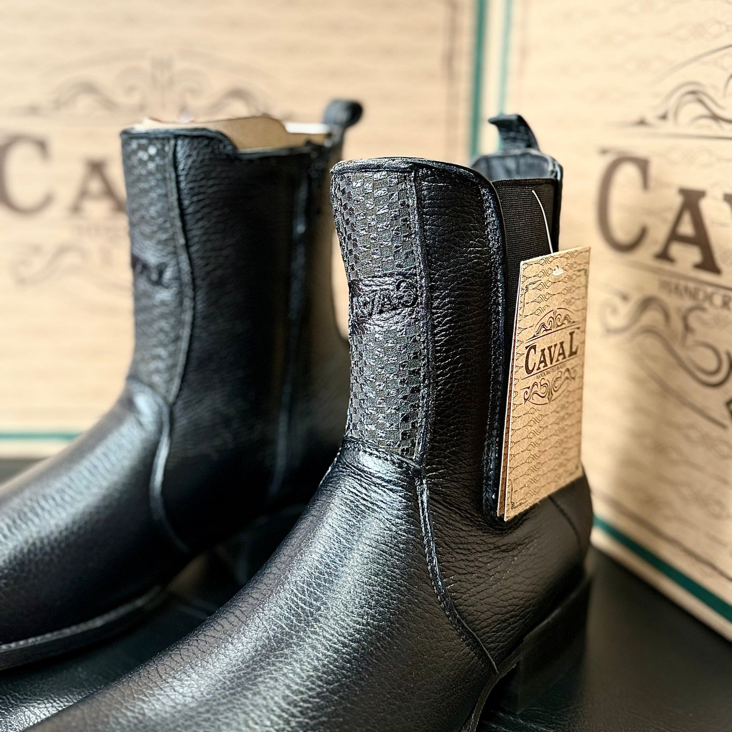 Black leather boots with a visible brand label on a wooden surface.
